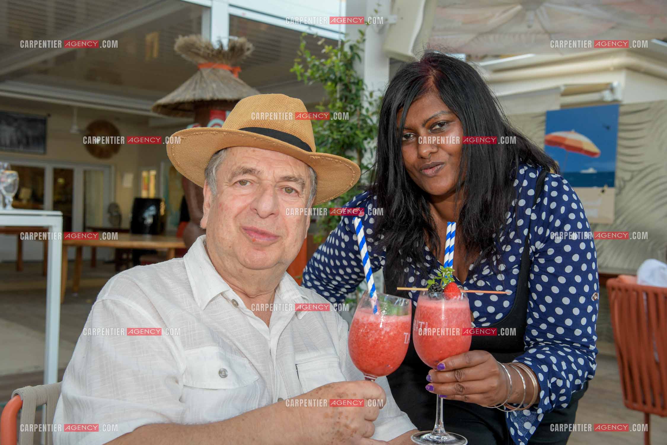 Paul-Loup Sulitzer lors d'une ballade sur le port de St Tropez. Ici en terrasse du bar de plage le " TAHAITI “  avec sa compagne  Supriya Answya Devi Rathoar.  ( Exclusif )